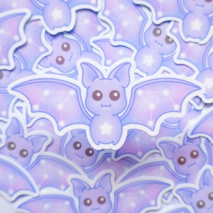 May include: A close-up of a stack of purple and white bat stickers with a constellation design. The bats have a cute cartoon style with big eyes and a star on their chest.
