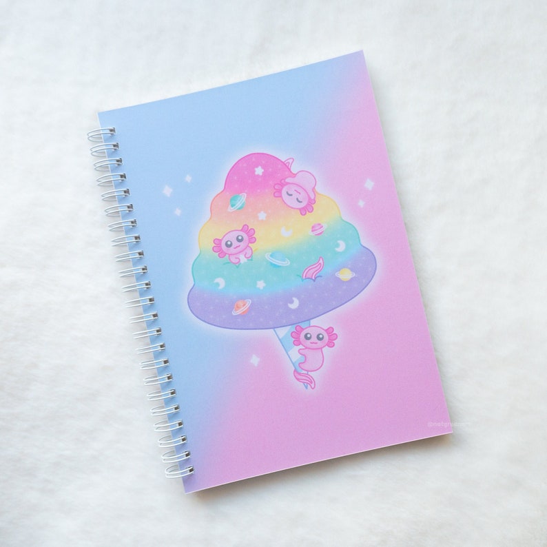 May include: A pink and blue spiral bound notebook with a rainbow cotton candy cloud with axolotls and stars on the cover.
