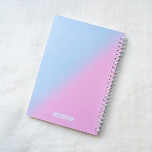 May include: A pink and blue ombre spiral bound notebook with the text "natgreenart" printed on the cover.