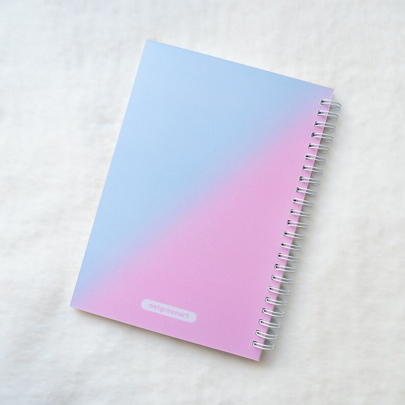 May include: A pink and blue ombre spiral bound notebook with the text "natgreenart" printed on the cover.