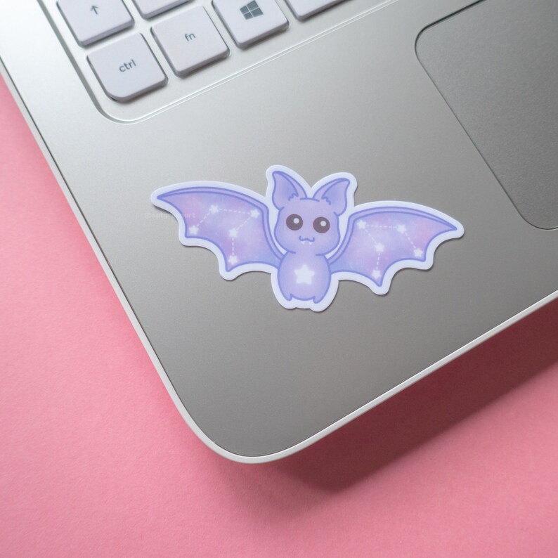 May include: A purple and white bat sticker with a constellation design on its wings. The sticker is on a silver laptop.