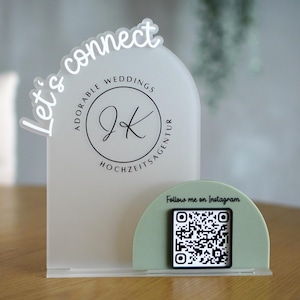 Può includere: Un cartello nuziale in acrilico trasparente con la scritta "Let's connect" e un logo. Il cartello ha una base verde menta con un codice QR e la scritta "Follow me on Instagram".