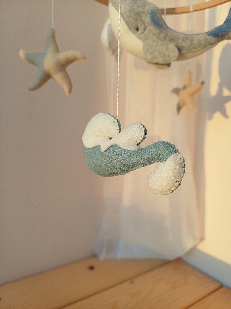 K&ouml;nnte beinhalten: Ein Baby-Mobile mit einem blauen Wal, einem Seestern und einem Seepferdchen. Das Mobile ist aus Filz gefertigt und h&auml;ngt an einem Holzring.