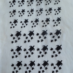 May include: A sheet of black vinyl stickers featuring multiple silhouettes of sea turtles of varying sizes. The turtles are arranged in rows, with the largest turtles in the center and smaller turtles surrounding them.