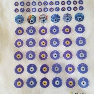 May include: A sheet of blue and white evil eye stickers. The stickers are in various sizes and shapes, including round, oval, and teardrop. Some of the stickers have a yellow center, while others have a white center. The stickers are arranged in rows and columns on a white background. The text "Alistaresin Studio" is in the bottom right corner of the image.
