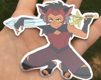 May include: A sticker featuring a cartoon character with red hair, a red and black outfit, and a sword. The character has a yellow eye and a red nose.