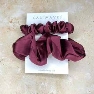May include: Two burgundy silk scrunchies on a white card with the text "CALIWAVES" and "100% Mulberry Silk".