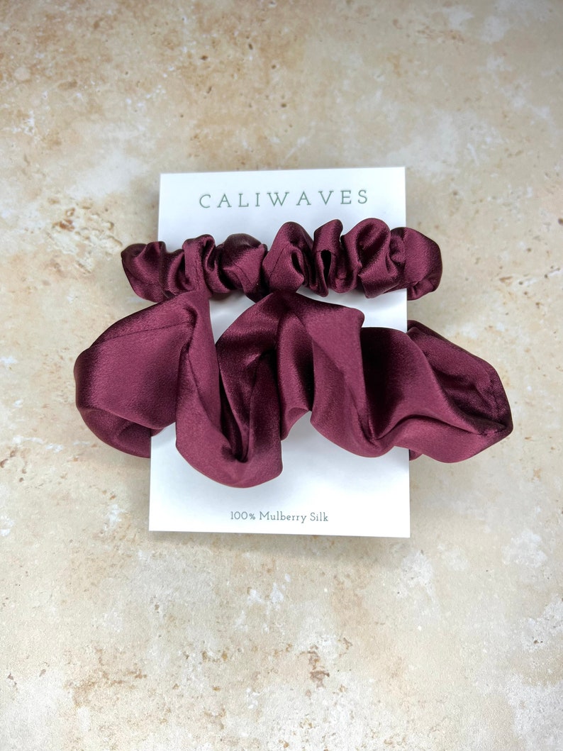 May include: Two burgundy silk scrunchies on a white card with the text "CALIWAVES" and "100% Mulberry Silk".