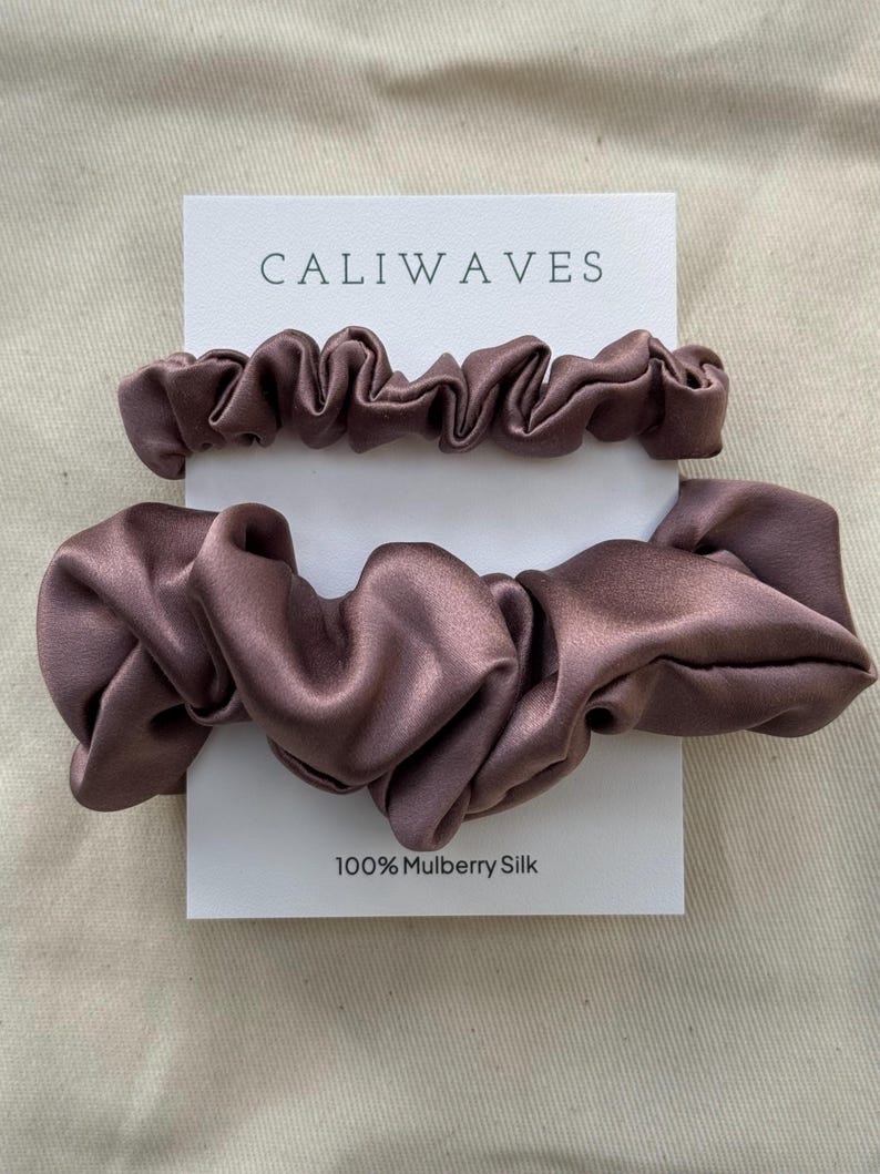 May include: Two brown satin scrunchies on a white card with the text "CALIWAVES" and "100% Mulberry Silk".