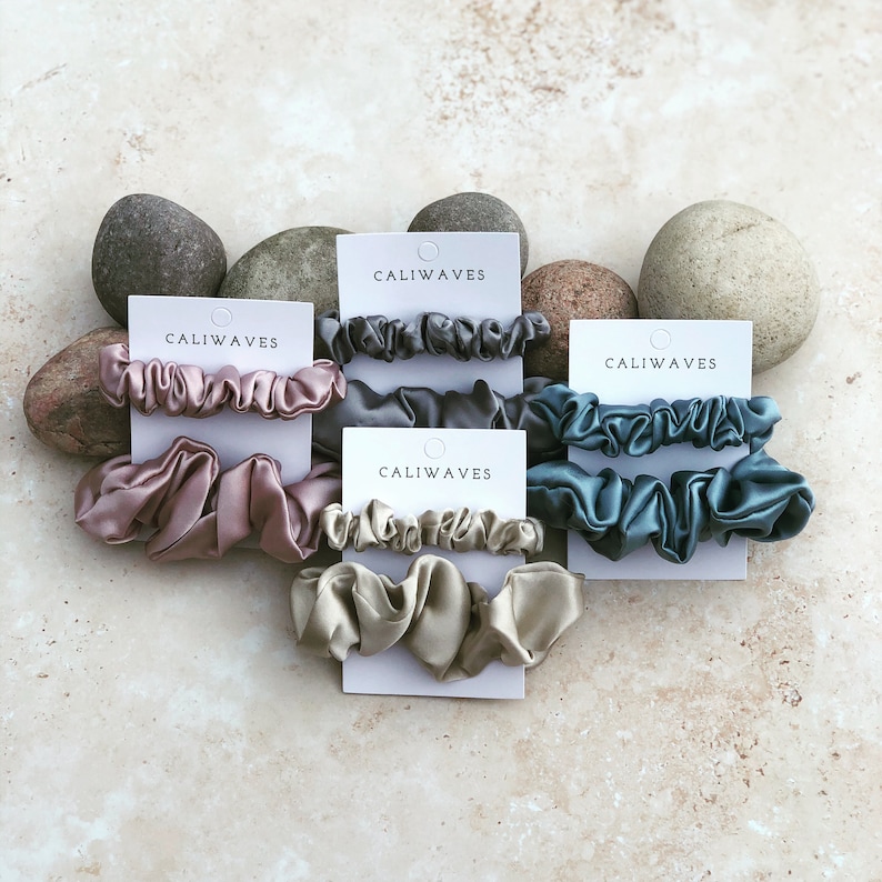 May include: Four sets of hair scrunchies in different colors, including dusty rose, gray, teal, and beige. Each set is packaged on a white card with the brand name "CALIWAVES" printed on it.