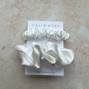 May include: Two white silk scrunchies on a white card with the text "CALIWAVES" and "100% Mulberry Silk".