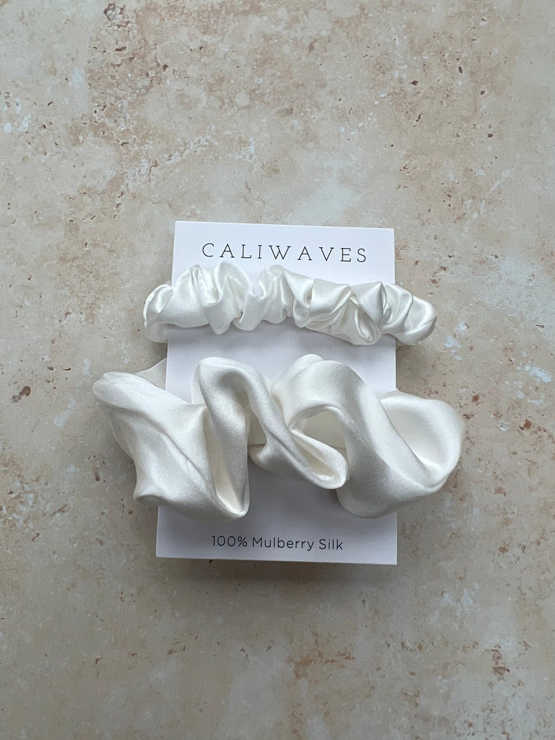 May include: Two white silk scrunchies on a white card with the text "CALIWAVES" and "100% Mulberry Silk".