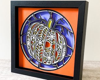 May include: A black framed picture with a 3D paper cut-out of a pumpkin with a spiderweb design. The pumpkin is orange and yellow with a purple and blue background.
