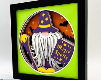 May include: A 3D papercraft gnome wearing a purple and yellow hat with stars, holding a book that says "Magic Spells". The gnome is surrounded by bats and stars in a green frame.