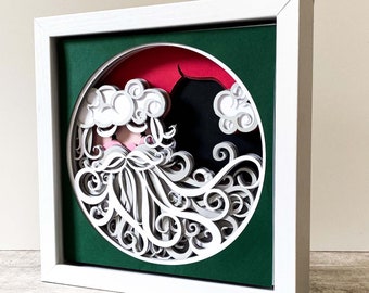May include: A white papercraft Santa Claus with a red hat and white beard in a green frame. The Santa is in a circle with a red background and white swirls.