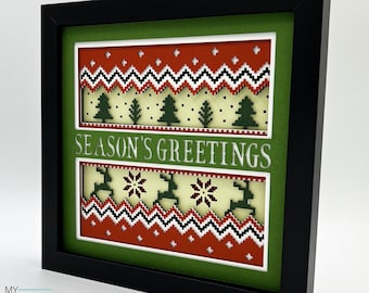 May include: A framed 3D papercraft design with a green background and a red, white, and black patterned sweater design. The text "Season's Greetings" is in the center of the design.