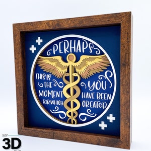 May include: A framed 3D papercraft design with a blue background and a white circle containing a gold caduceus with wings, surrounded by the text "Perhaps this is the moment for which you have been created".