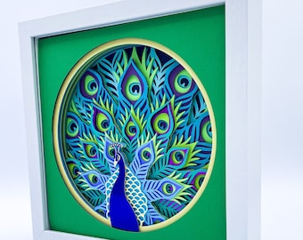 May include: A white frame with a green mat and a circular cutout featuring a blue and green peacock with its tail feathers spread out.