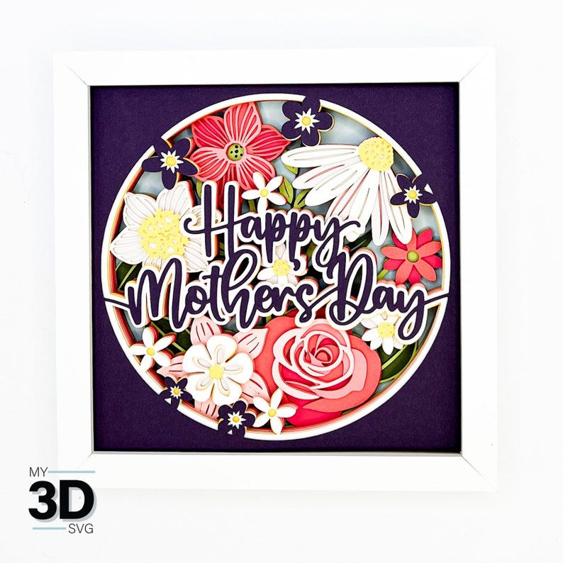 Puede incluir: Un marco blanco con un fondo morado y un c&iacute;rculo de flores de papel en tonos de rosa, blanco y amarillo. El texto "Happy Mother's Day" est&aacute; en el centro del c&iacute;rculo.
