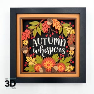 Può includere: Un'opera d'arte in carta 3D incorniciata con le parole "AUTUMN whispers" in scrittura bianca. L'opera presenta una ghirlanda di foglie autunnali, ghiande e fiori nei toni del rosso, arancione, giallo e verde, su sfondo nero.