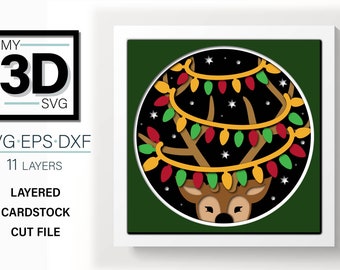 May include: A layered papercraft design of a reindeer with a string of Christmas lights around its antlers. The reindeer is looking at the viewer with a surprised expression. The background is a dark green color with white stars.