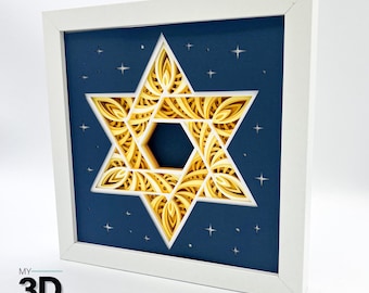 May include: A white frame with a blue background and a gold, intricate, 3D paper cut-out of a Star of David.