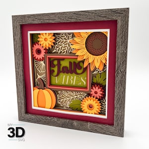 May include: A framed 3D paper art piece with a fall theme. It features a pumpkin, sunflowers, and the words "Fall Vibes" in a layered design. The frame is a rustic gray, and the background is a deep red.