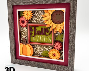 May include: A framed 3D paper art piece with a fall theme. It features a pumpkin, sunflowers, and the words "Fall Vibes" in a layered design. The frame is a rustic gray, and the background is a deep red.