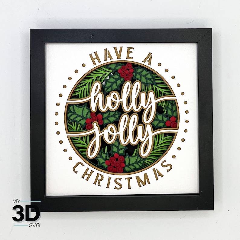 May include: A black framed picture with a white background and a gold circle with the text "Have a holly jolly Christmas" in white lettering. The circle is surrounded by green holly leaves and red berries.