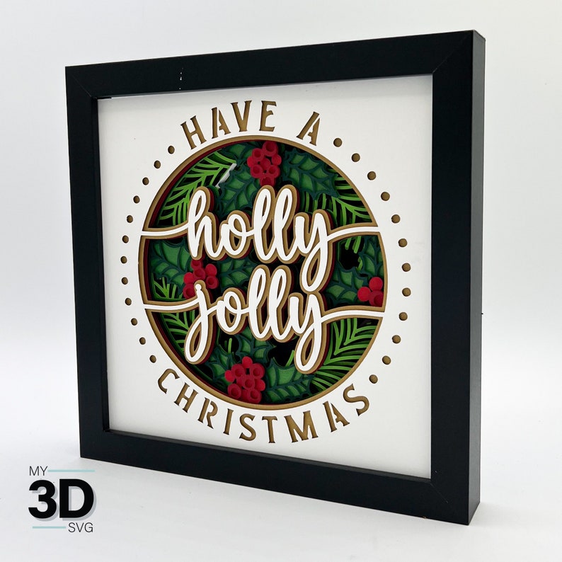 May include: A black framed 3D papercraft with a white background and gold lettering that reads "Have a holly jolly Christmas" surrounded by green holly leaves and red berries.