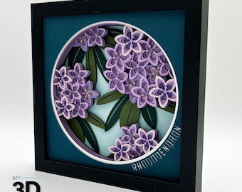 Könnte beinhalten: Ein gerahmtes Papierkunstwerk mit einem 3D-Papier-Schnittdesign einer Rhododendron-Blume in Violett- und Rosatönen. Die Blume ist von grünen Blättern umgeben und der Text "MY RHODODENDRON" ist am unteren Rand des Designs sichtbar.