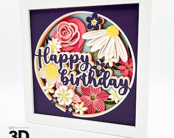 May include: A 3D paper craft with a purple background and a circle of layered paper flowers in shades of pink, yellow, and white. The text "Happy Birthday" is layered in purple on top of the flowers.