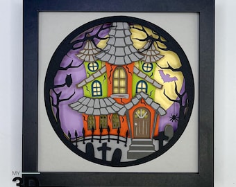 May include: A 3D papercraft Halloween scene with a spooky house, a full moon, and a bat flying in the night sky. The house is decorated with orange, green, and gray colors. The scene is framed in a black frame.