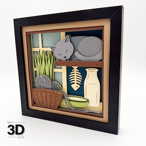 May include: A framed 3D paper art piece featuring a sleeping gray cat on a shelf, a basket with yarn, and a fish skeleton. The artwork includes a window design with green grass and a cream-colored bottle. The frame is black.