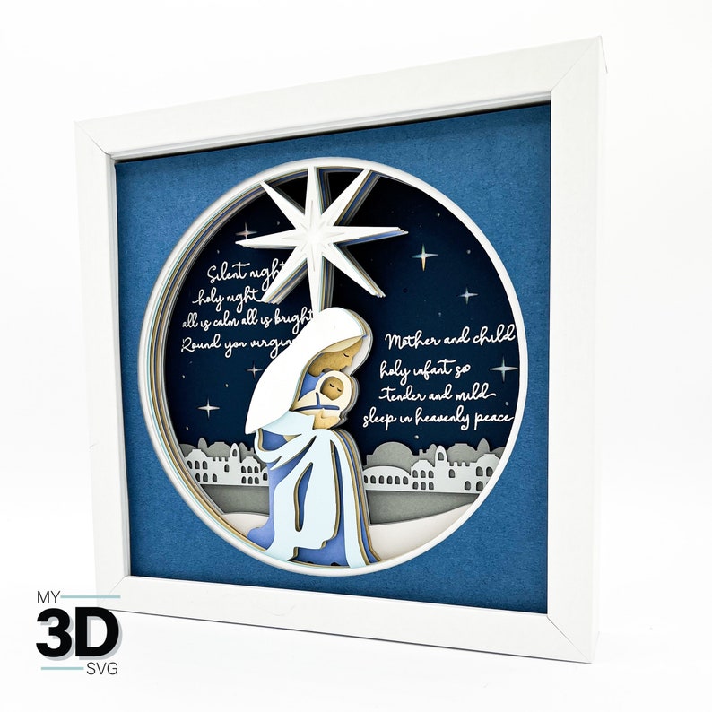 May include: A white framed 3D layered paper art piece depicting the nativity scene with Mary and baby Jesus. The scene is set against a blue background with a large star and the text "Silent night, holy night, all is calm, all is bright, Round you virgin, Mother and child, holy infant so, tender and mild, sleep in heavenly peace."
