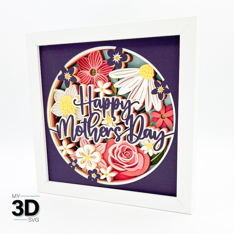 Puede incluir: Un marco blanco con un fondo morado y un c&iacute;rculo de flores de papel en tonos de rosa, blanco y amarillo. Las flores est&aacute;n superpuestas para crear un efecto 3D. El texto "Happy Mother's Day" est&aacute; escrito en una fuente decorativa.