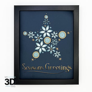 May include: A framed paper craft with a blue background and a gold star design. The star is made up of multiple layers of paper flowers and circles. The text "Seasons Greetings" is written in gold lettering below the star.