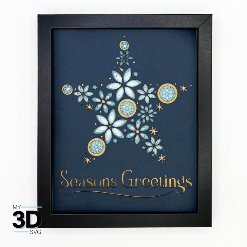 May include: A framed paper craft with a blue background and a gold star design. The star is made up of multiple layers of paper flowers and circles. The text "Seasons Greetings" is written in gold lettering below the star.