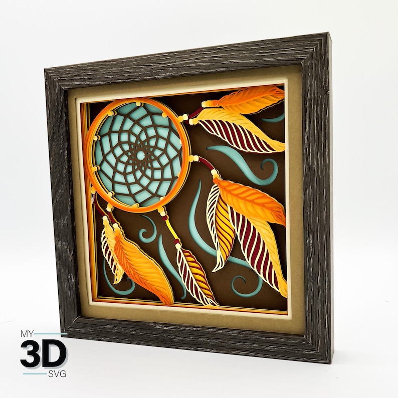 K&ouml;nnte beinhalten: Ein gerahmtes 3D-Papiermodell eines Traumf&auml;ngers mit orangefarbenen und roten Federn. Der Traumf&auml;nger ist aus Papier gefertigt und hat ein blaues und wei&szlig;es Design. Der Rahmen ist aus braunem Holz.