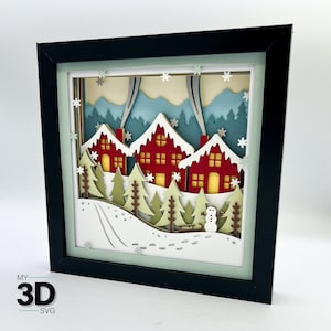 May include: A 3D papercraft scene of a winter village with three red houses, snow-covered trees, and a snowman in a black frame.