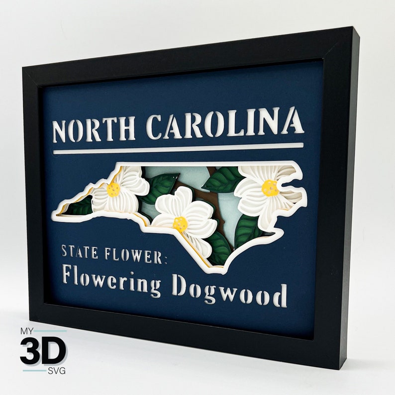 May include: A 3D papercraft of the state of North Carolina with the state flower, the flowering dogwood, in the shape of the state. The papercraft is framed in black and has a blue background with the words "North Carolina" and "State Flower: Flowering Dogwood" in white.