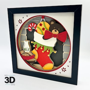 Puede incluir: Una escena de papelcraft 3D de una chimenea con una media colgada del manto. La media está llena de un osito de peluche con una pajarita roja, un bastón de caramelo y una bola amarilla con estrellas rojas. Una botella de leche y galletas están sobre una mesa frente a la chimenea.