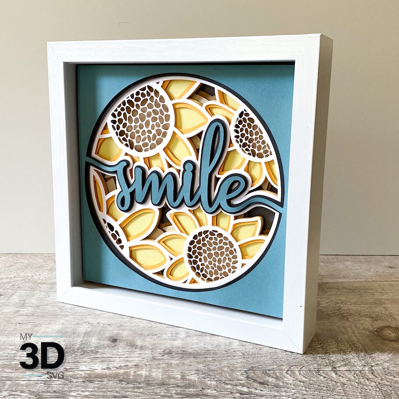 May include: White framed wall art with a blue background and a circle of yellow and brown sunflowers with the word "smile" in blue lettering.