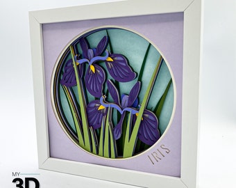 May include: A white frame with a light purple mat surrounding a circular cutout of a 3D paper art design of purple iris flowers with yellow centers and green leaves. The text "IRIS" is written in gold lettering at the bottom of the cutout.