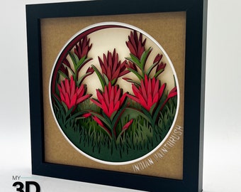Puede incluir: Una obra de arte en papel enmarcada que representa un grupo de flores rojas de pincel indio en un diseño circular. Las flores están superpuestas y tienen un efecto 3D. El fondo es un papel marrón claro con el texto "Indian Paintbrush" escrito en blanco.