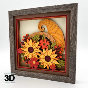 May include: A framed 3D artwork depicting a cornucopia filled with sunflowers and autumnal flowers. The wooden frame has a grey finish. The color scheme includes orange, yellow, red, and green hues. The artwork is a decorative piece.