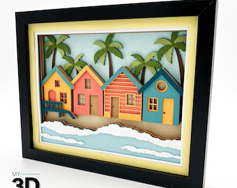 May include: A framed 3D paper art piece depicting a beach scene with colorful beach huts, palm trees, and ocean waves. The huts are painted in shades of yellow, pink, orange, and blue. The artwork is set against a light blue background and framed in black.