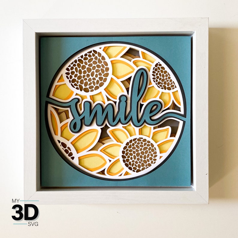 May include: A white frame with a blue background and a circle of sunflowers with the word "smile" in the center. The sunflowers are layered and have a 3D effect.