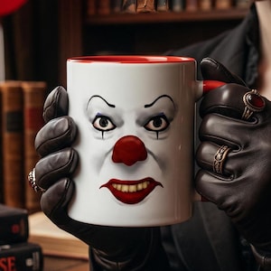 Peut inclure: Un mug en céramique blanche orné d'un graphisme détaillé représentant un visage de clown avec un nez rouge, un maquillage des yeux sombre et un large sourire montrant les dents. L'intérieur et l'anse du mug sont d'un rouge vif.
