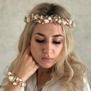 May include: A white and pink floral crown with small white flowers and pink accents. The crown is worn on a person's head.